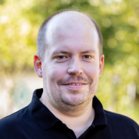 Rolf Korb, Mann mit leichtem Bart, lächelt und schwarzem Poloshirt.